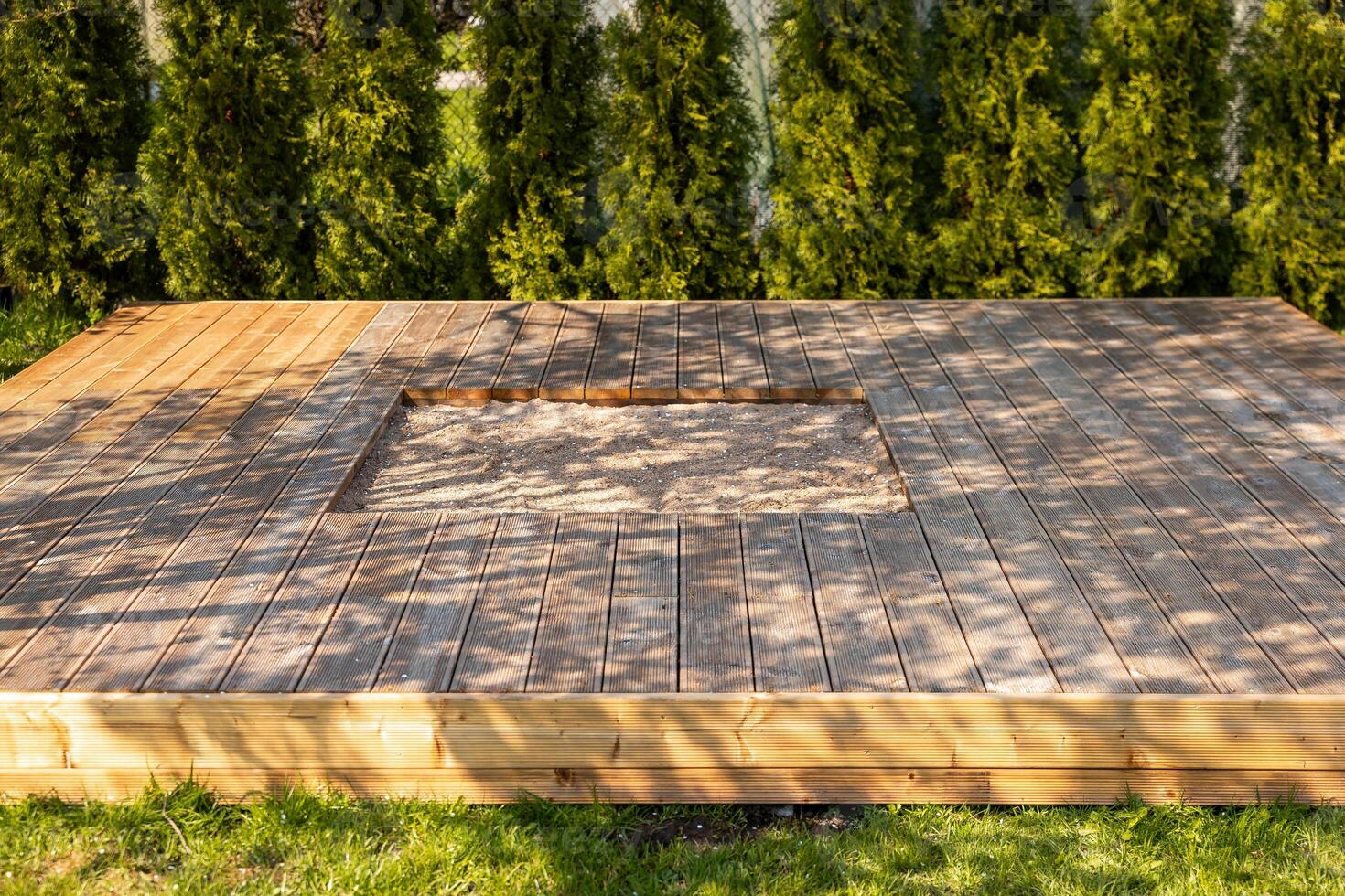 Wooden deck with central sandpit in a backyard setting, surrounded by trees and natural surroundings photo