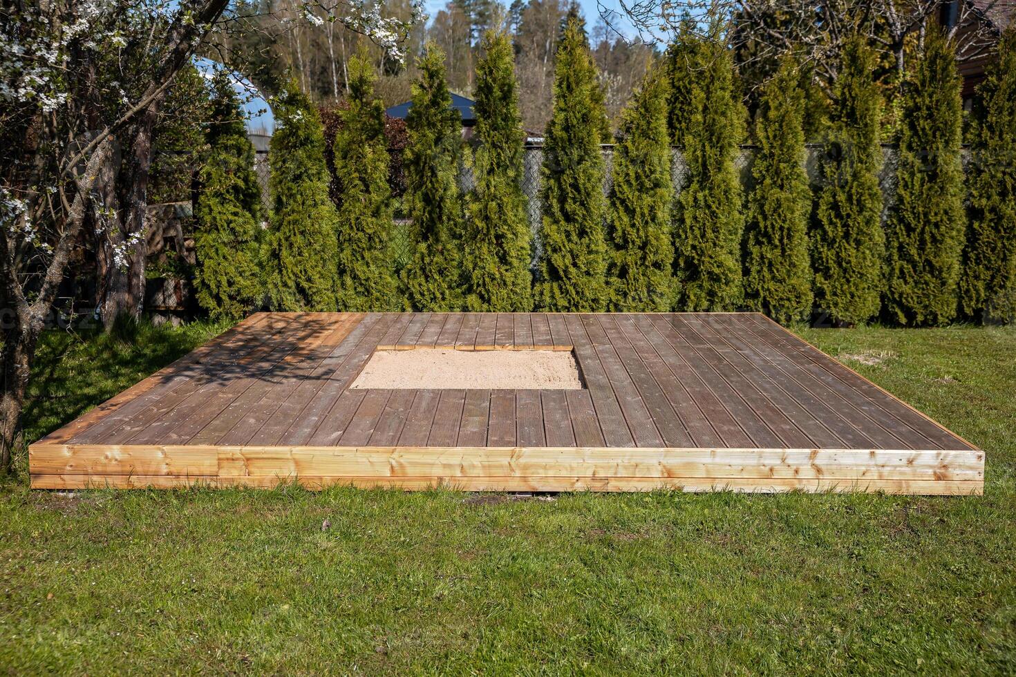 Wooden deck with a central sandpit in a sunny backyard, featuring a clean and simple design photo