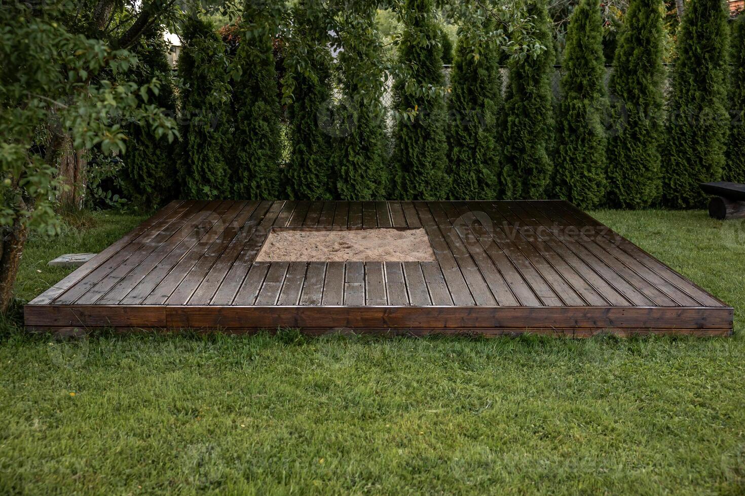 Wooden deck with central sandpit in a backyard setting, surrounded by trees and natural surroundings photo