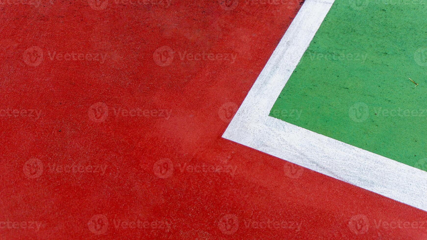 A close up of a tennis court corner, showing red and green surfaces divided by a white line. The textured ground and bold colors emphasize the courts geometry and minimalist design photo