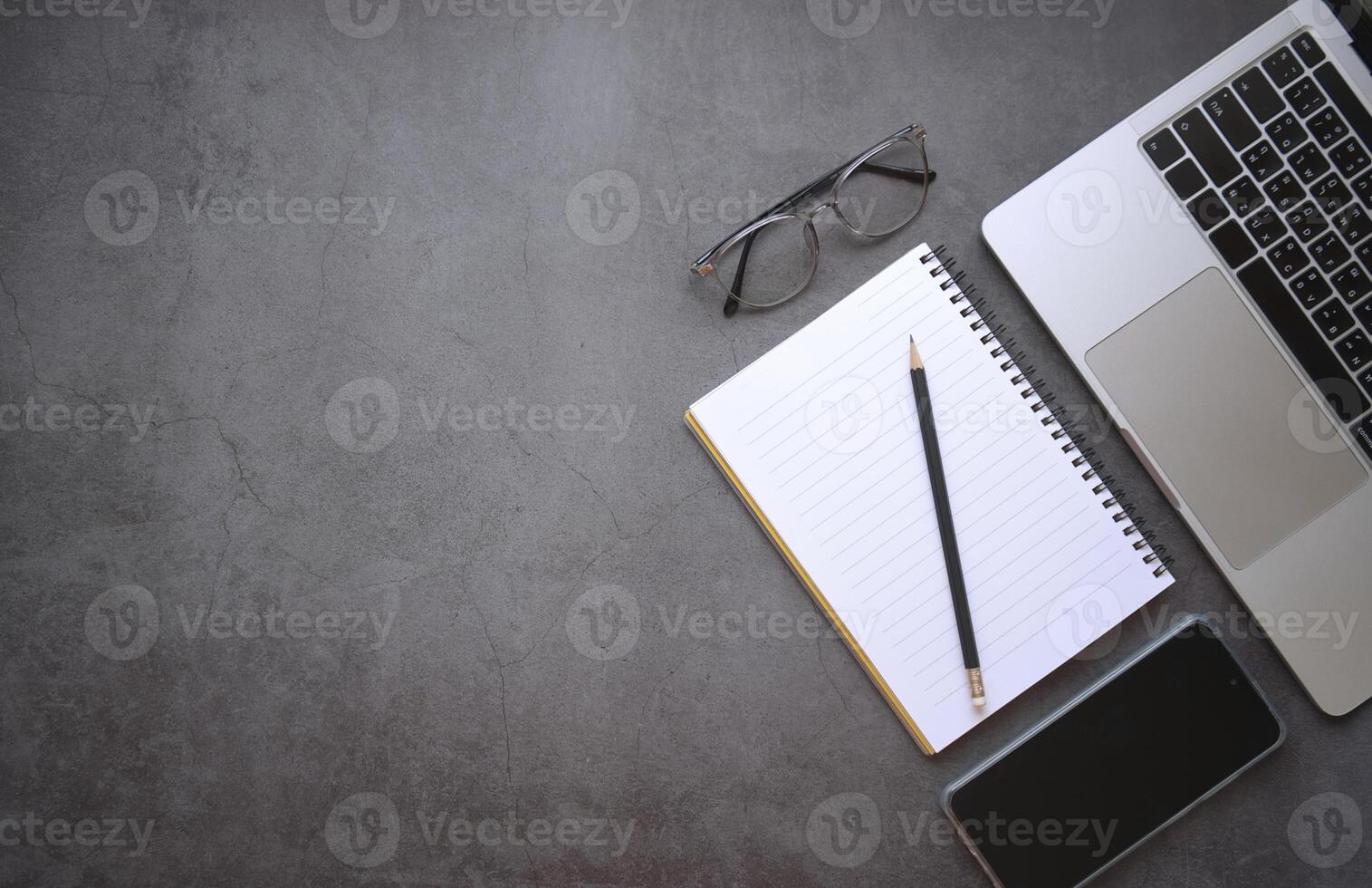 Flat lay top view laptop and mobile phone with notebook, pencil and glasses on light black color office desk photo