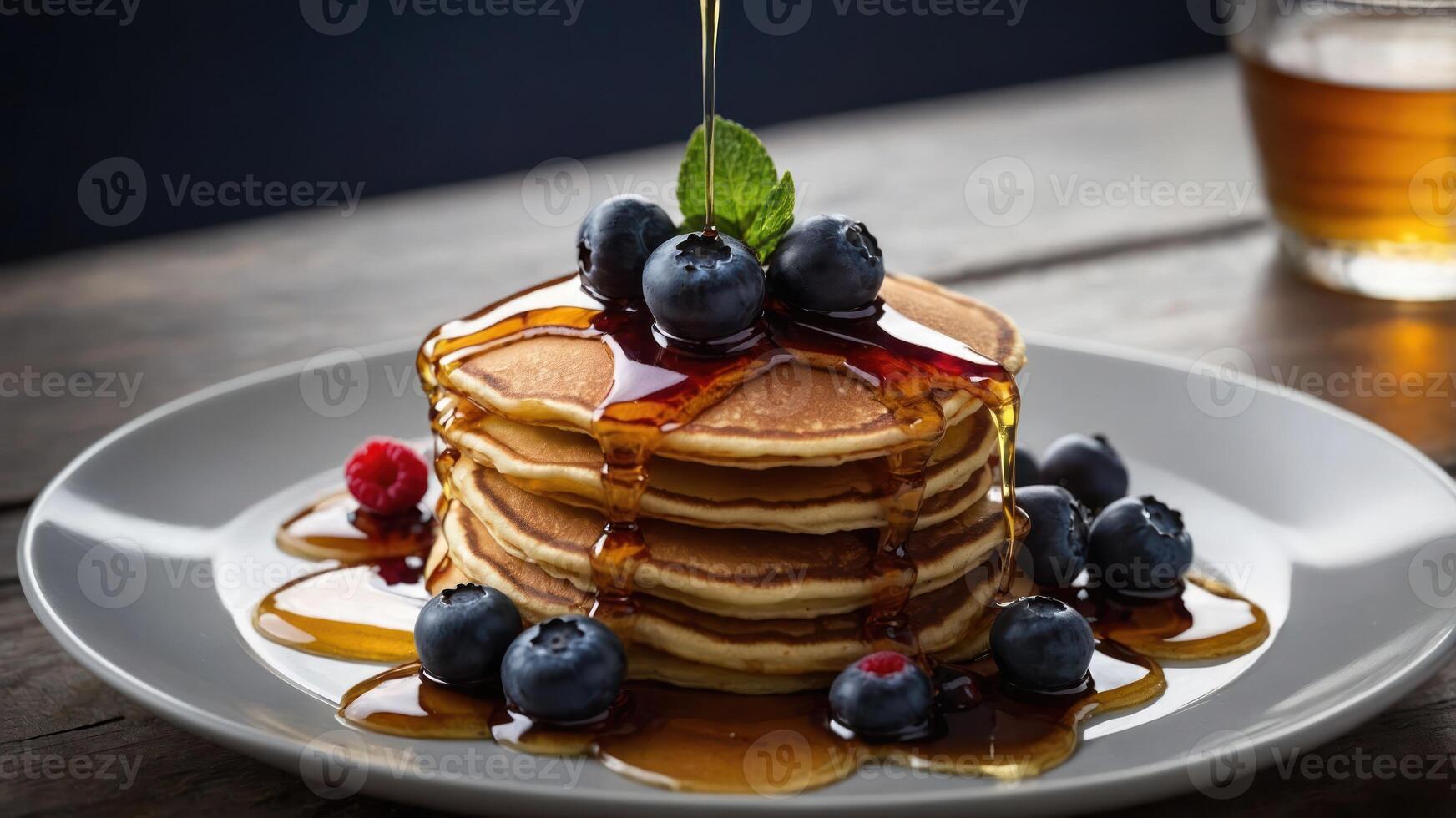 A stack of fluffy pancakes drizzled with syrup, topped with blueberries and mint. photo