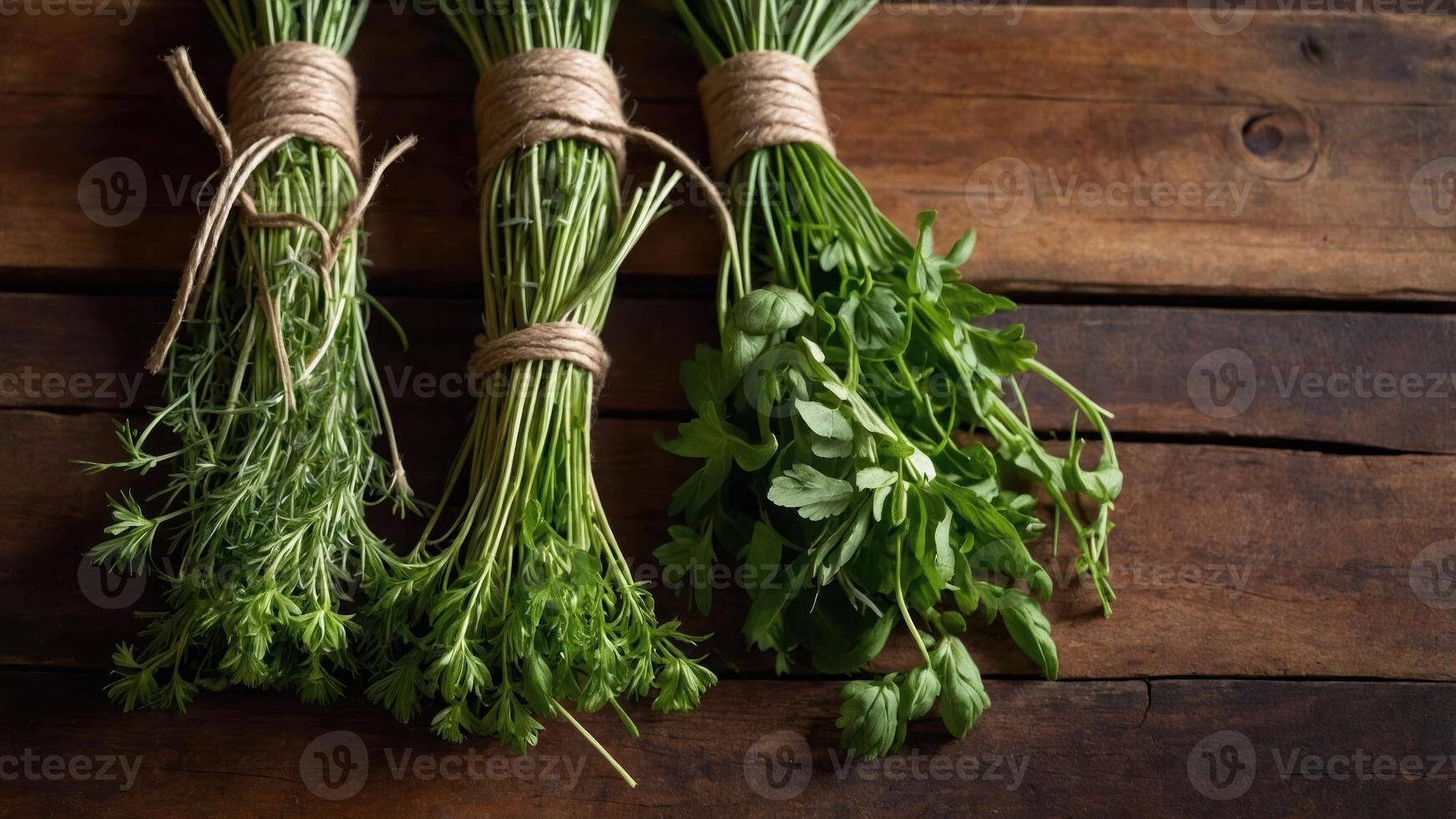 Three bundles of fresh herbs tied with twine on a wooden surface. photo