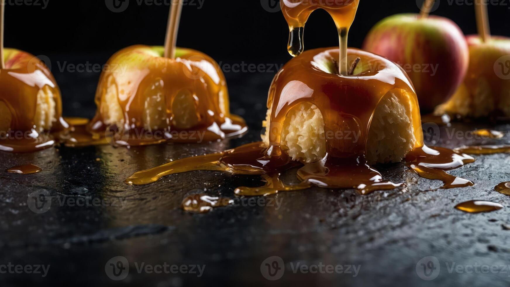 Caramel-coated apples on sticks with syrup drizzling, set against a dark background. photo