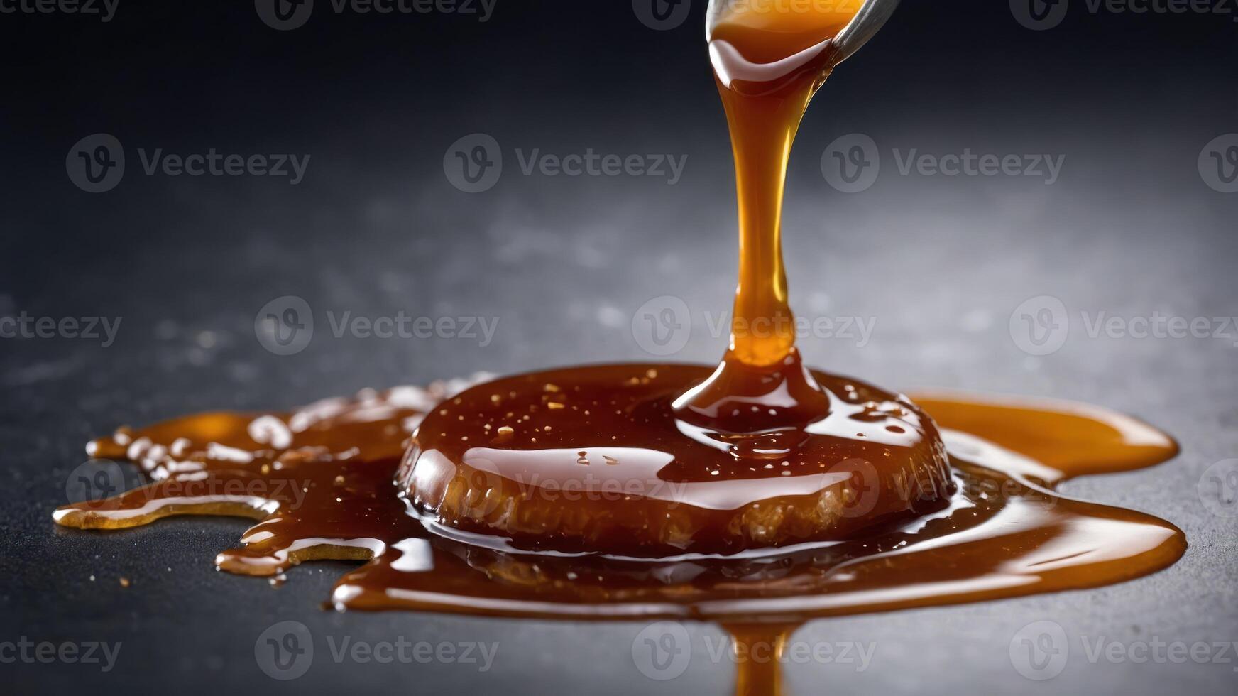 A glossy caramel sauce drips from a spoon, pooling on a dark surface. photo