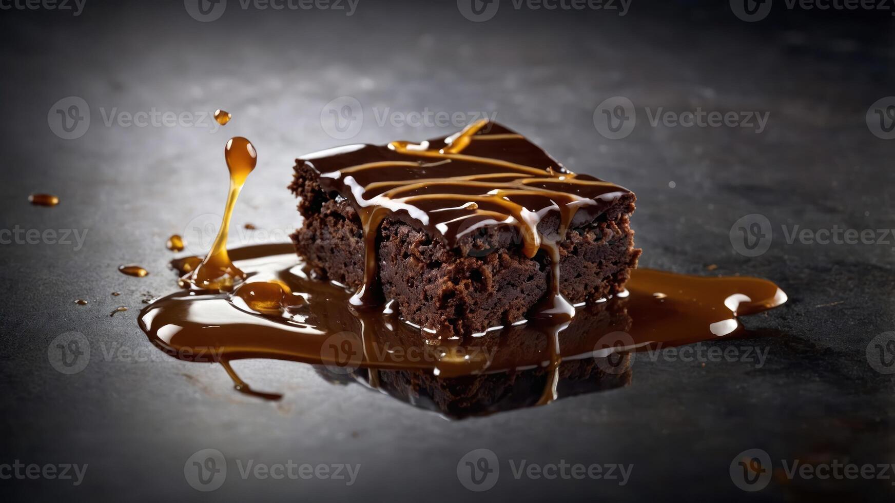 A rich chocolate brownie drizzled with caramel sauce on a dark surface. photo