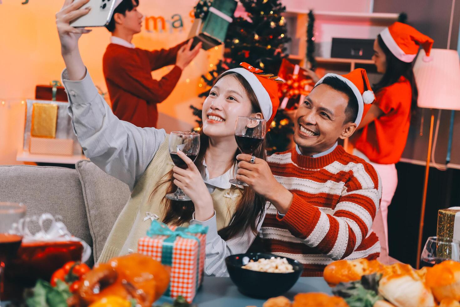 Group of happy Asian friends celebrating Christmas and decorate the Christmas tree indoors. Beauty woman with Christmas Gifts. New Year party. Woman hands decorate Christmas tree red ball, bauble. photo