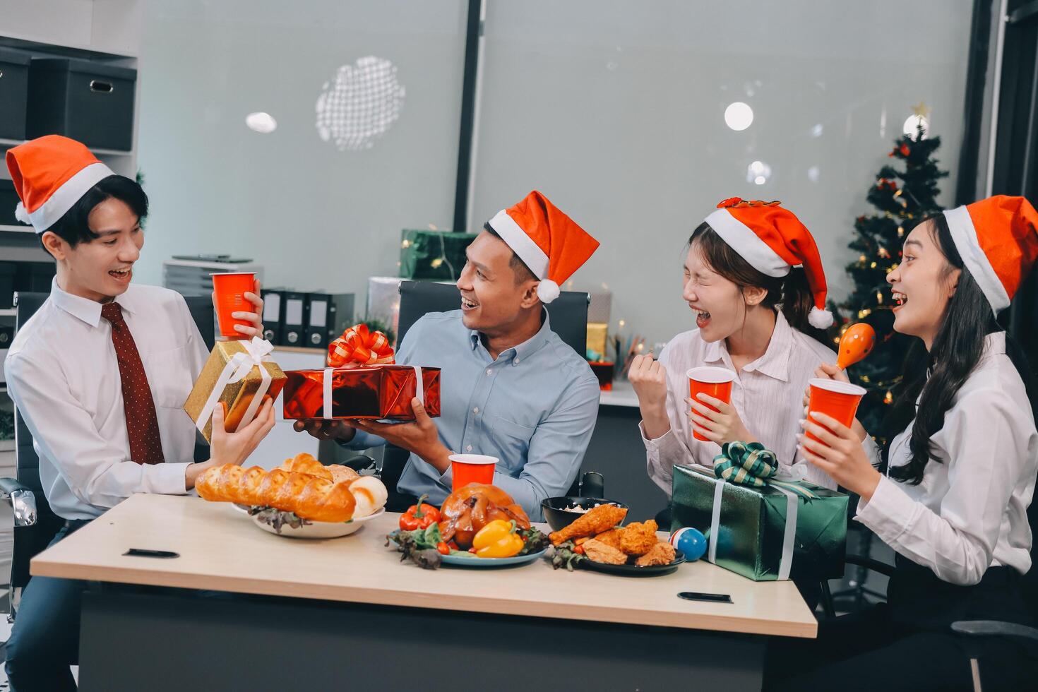 full length view of a group of business team wearing red Santa hat and exchange gift box together in the office for Christmas. photo