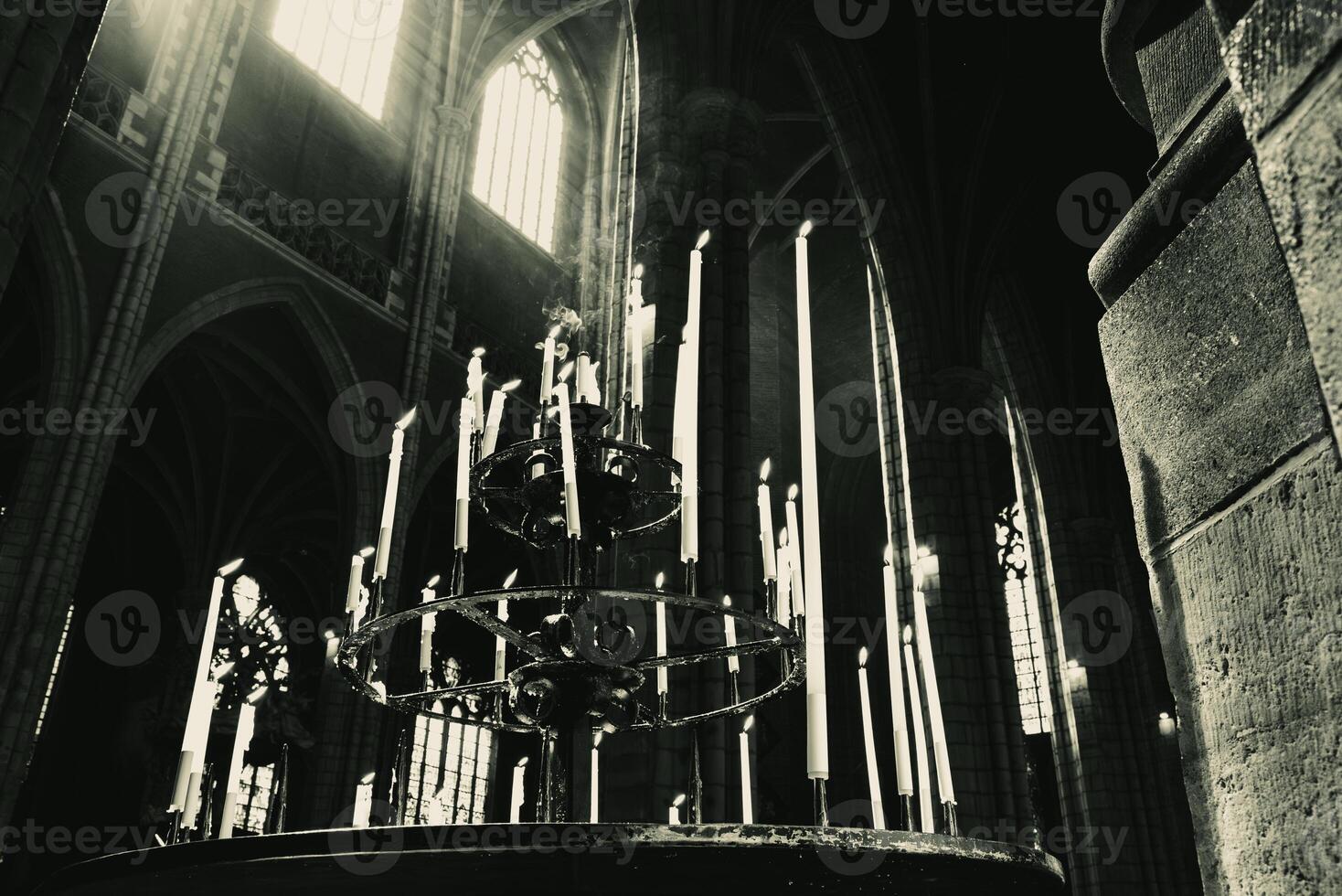 Desaturated tall candles in the dark cathedral under the light from the windows photo