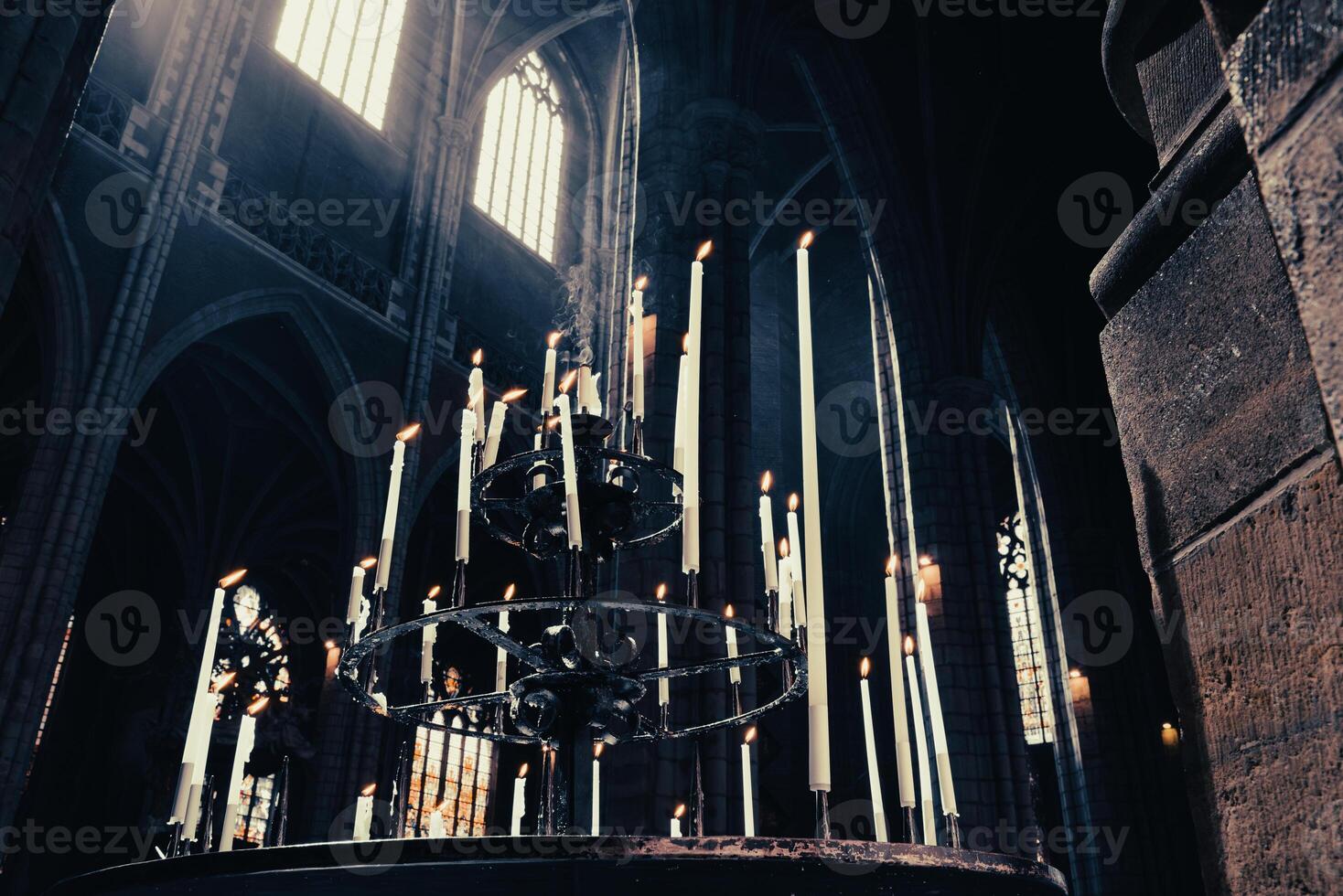 Desaturated tall candles in the dark cathedral under the light from the windows photo