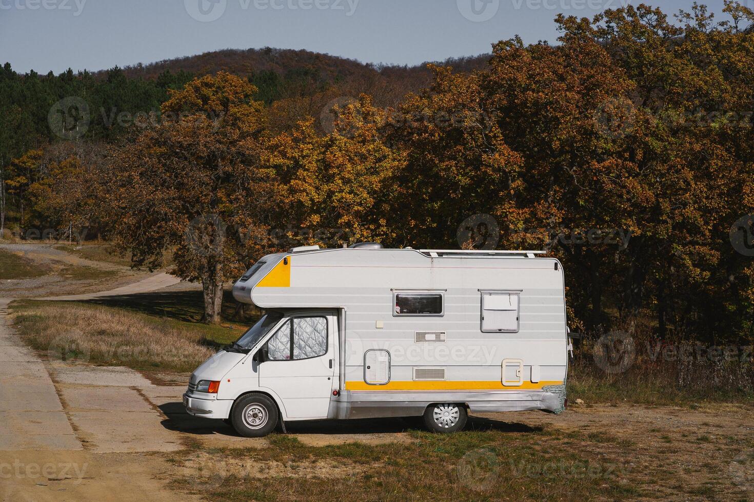 A retro camper parked beside a winding road in a colorful autumn landscape photo