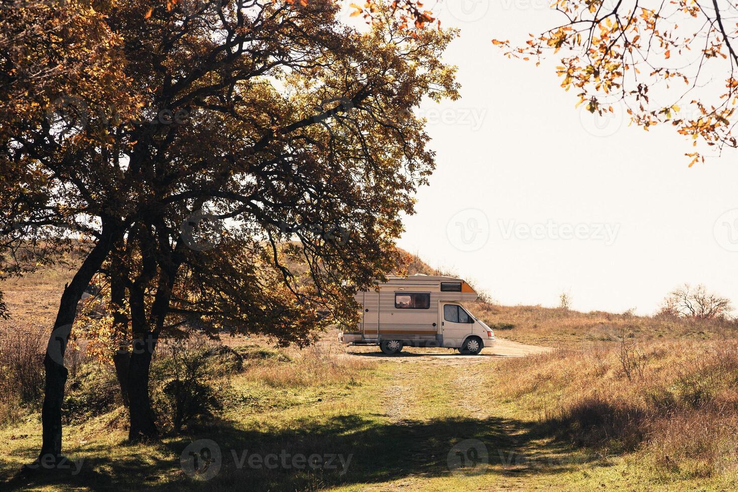 A serene camping spot with a camper van under autumn trees in the countryside during daylight hours photo