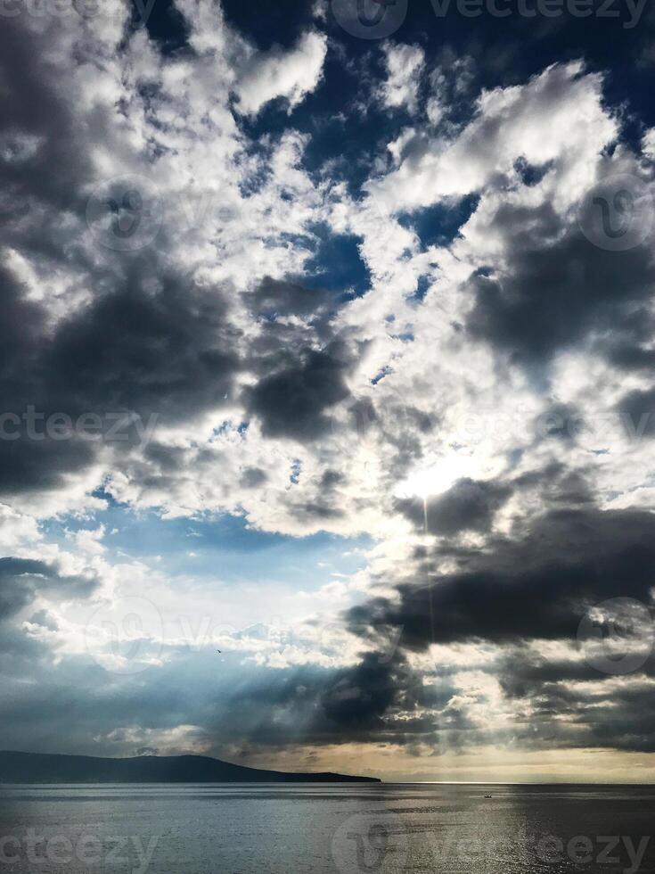 Dramatic cloudy sky over calm ocean with sunlight peeking through photo
