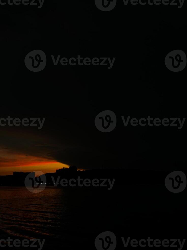Dramatic sunset over a silhouette city skyline by the water photo