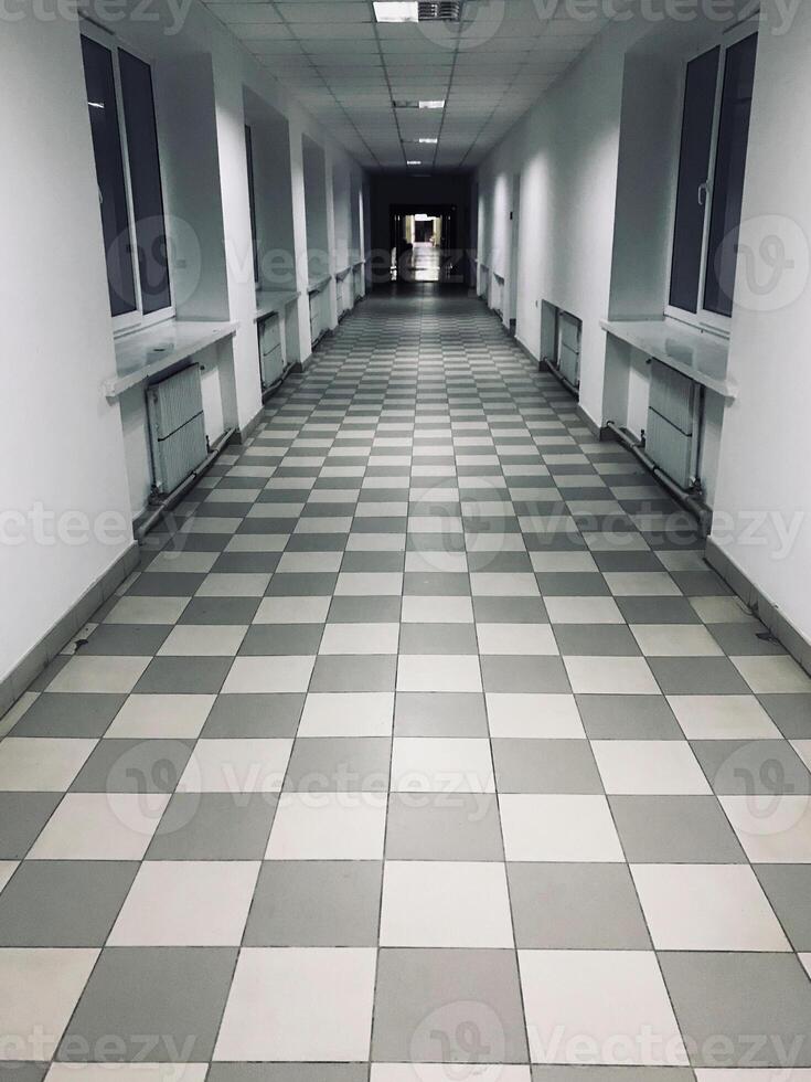 Long empty corridor with checkerboard tiled flooring and windows photo
