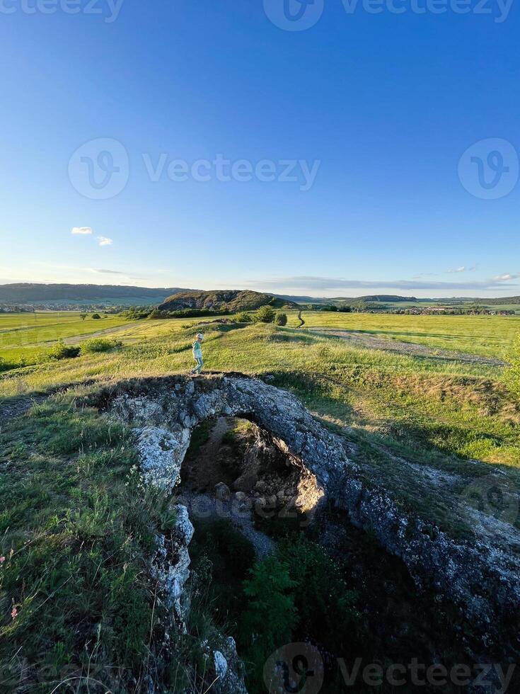 Solitary figure on natural rock bridge in a green landscape photo