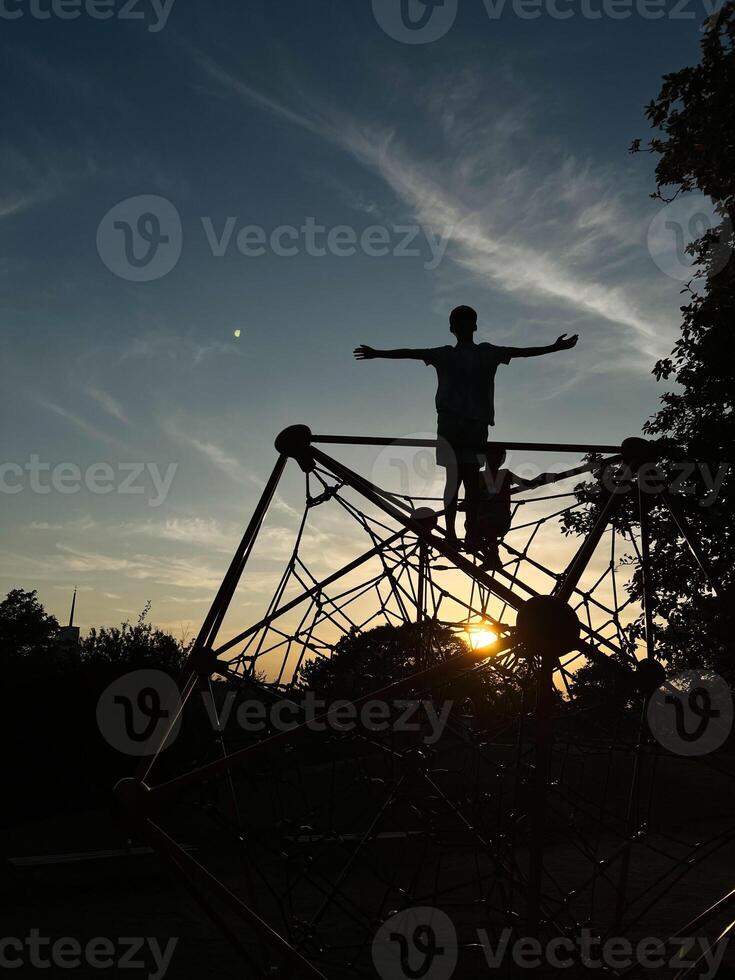 Silhouette of a child playing on a climbing frame at sunset photo
