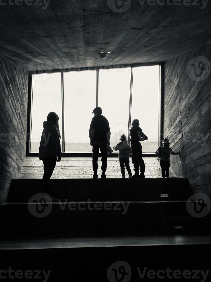 Family silhouette standing by large window in dark hallway photo