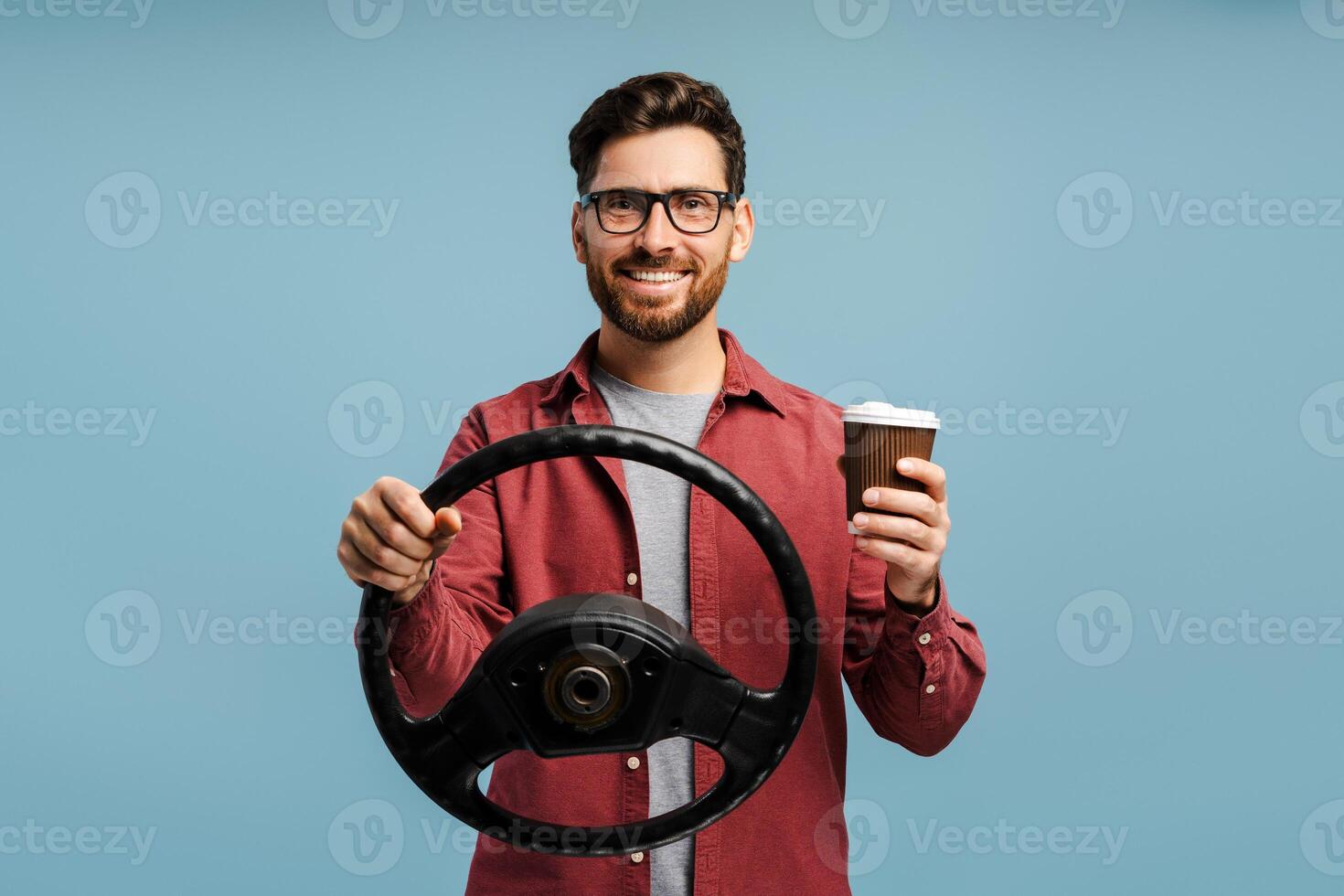 Handsome, smiling Latin man wearing eyeglasses holding steering wheel and paper cup with drink photo