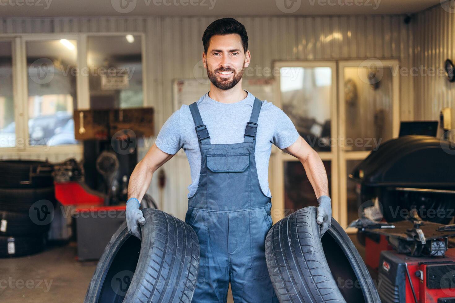 Handsome, smiling, bearded man wearing uniform, professional repairman holding tire, wheels photo