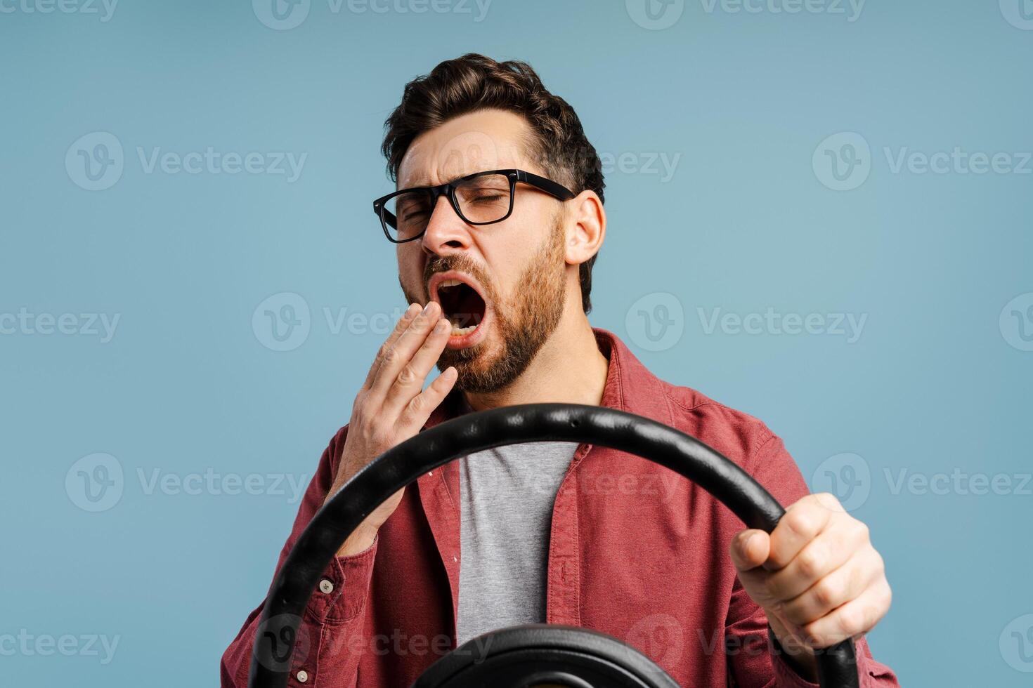 Portrait tired bearded, Latin man wearing eyeglasses yawning holding steering wheel photo