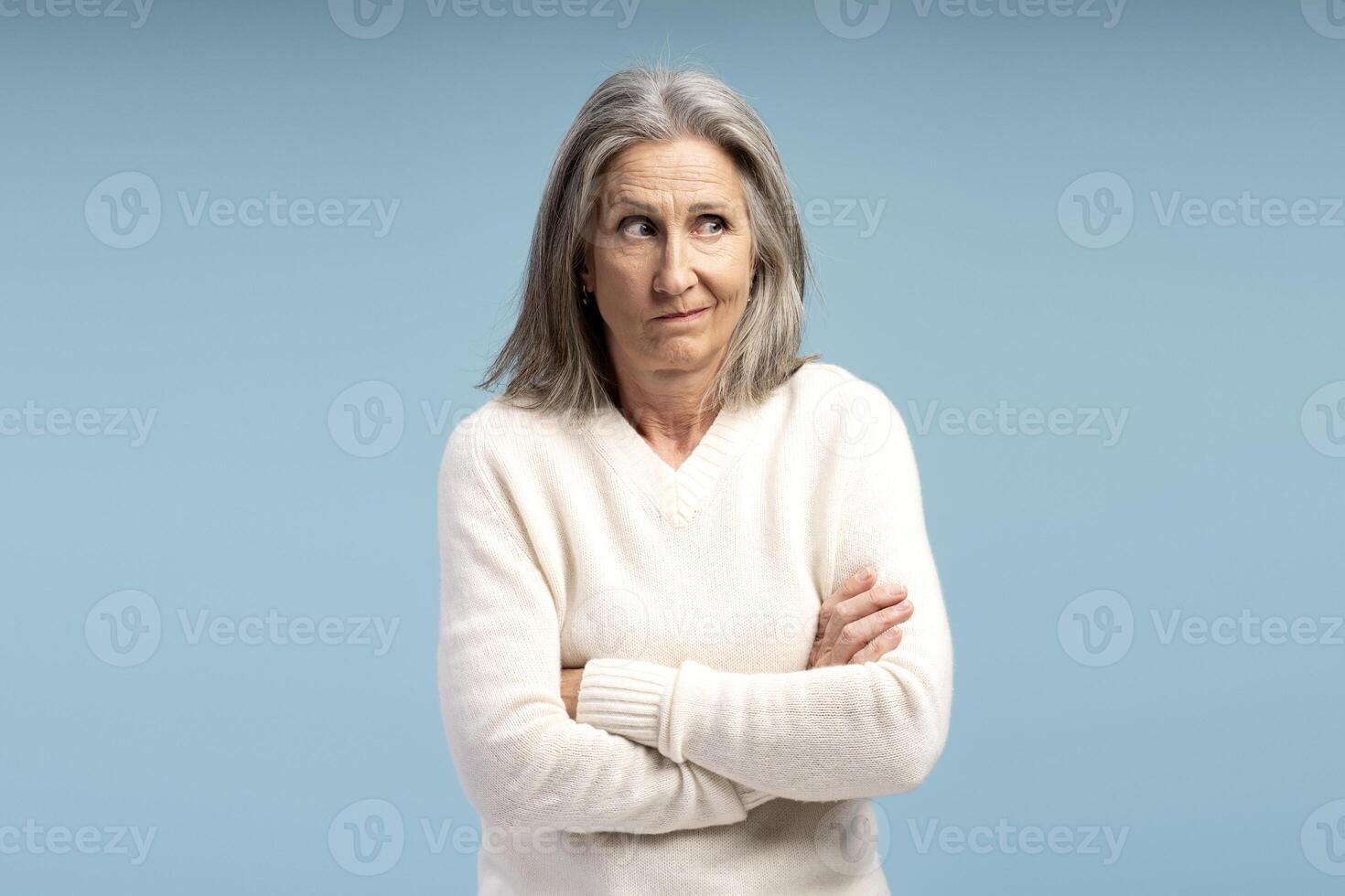 Portrait of senior, amazed, gray haired woman with crossed arms looking away. Advertisement concept photo