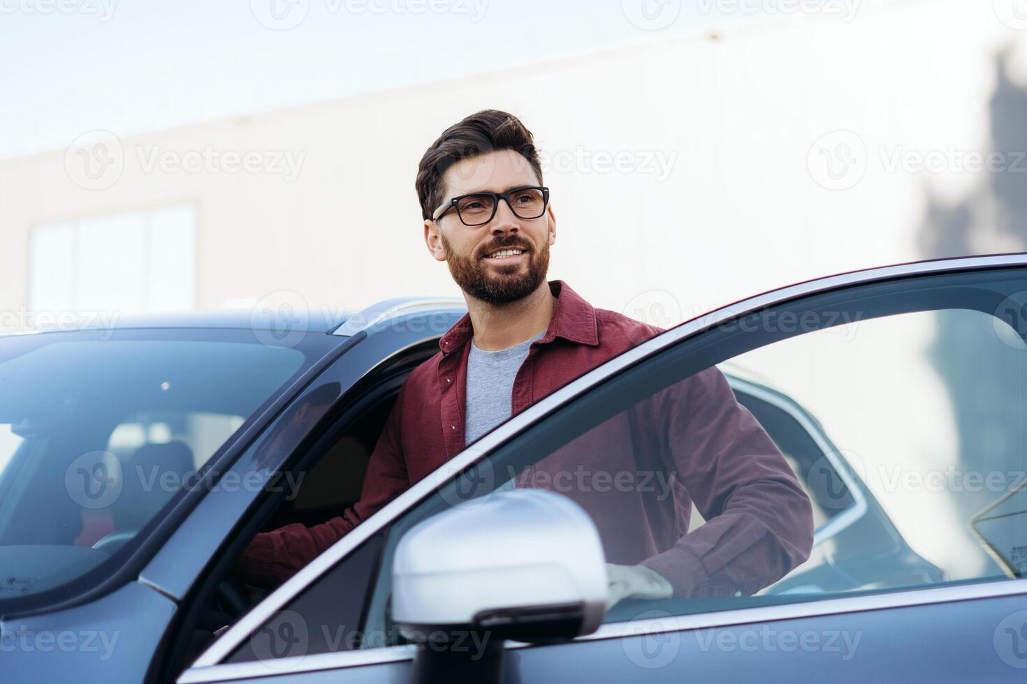 Handsome car owner, bearded Latin man wearing stylish eyeglasses, looking away, standing near car photo