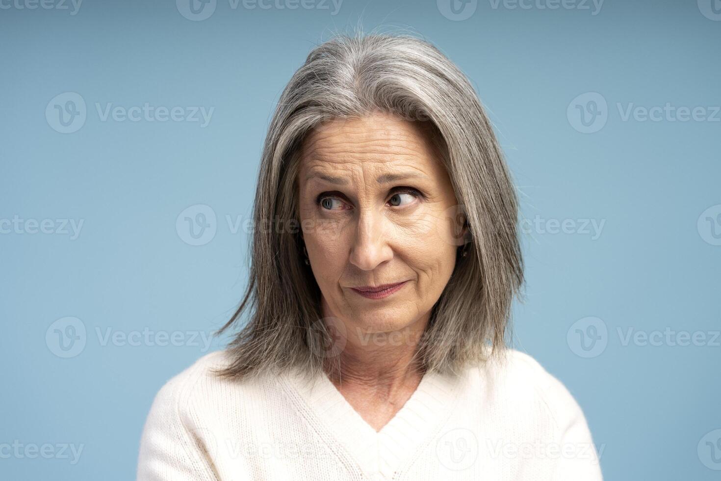 Portrait of pensive serious senior woman looking away, closeup, standing isolated on blue background photo