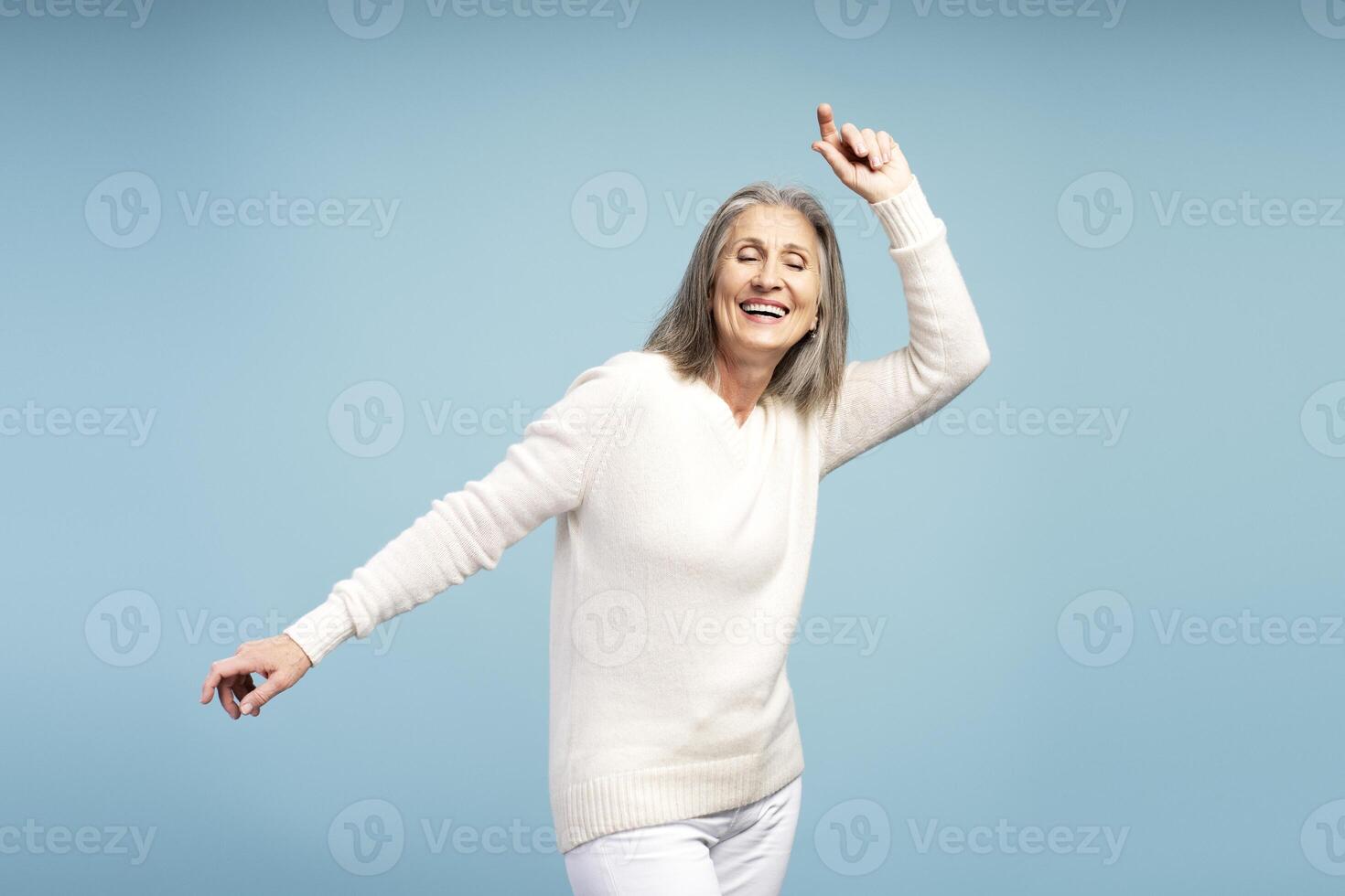 Happy, smiling senior woman with closed eyes, dancing, having fun, isolated on blue background photo