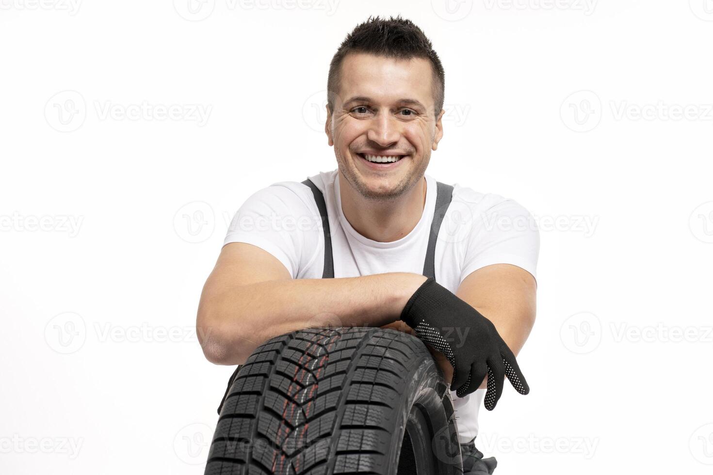Smiling mechanic leaning on winter tire on white background photo