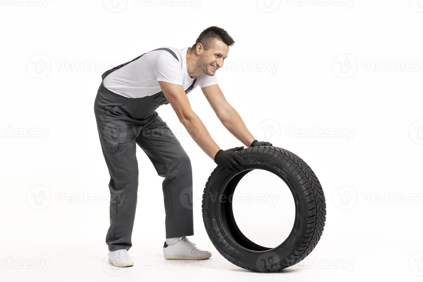 Mechanic pushing large tire on white background photo
