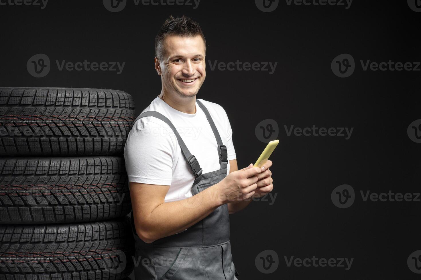 Mechanic using mobile phone next to stack of tires photo