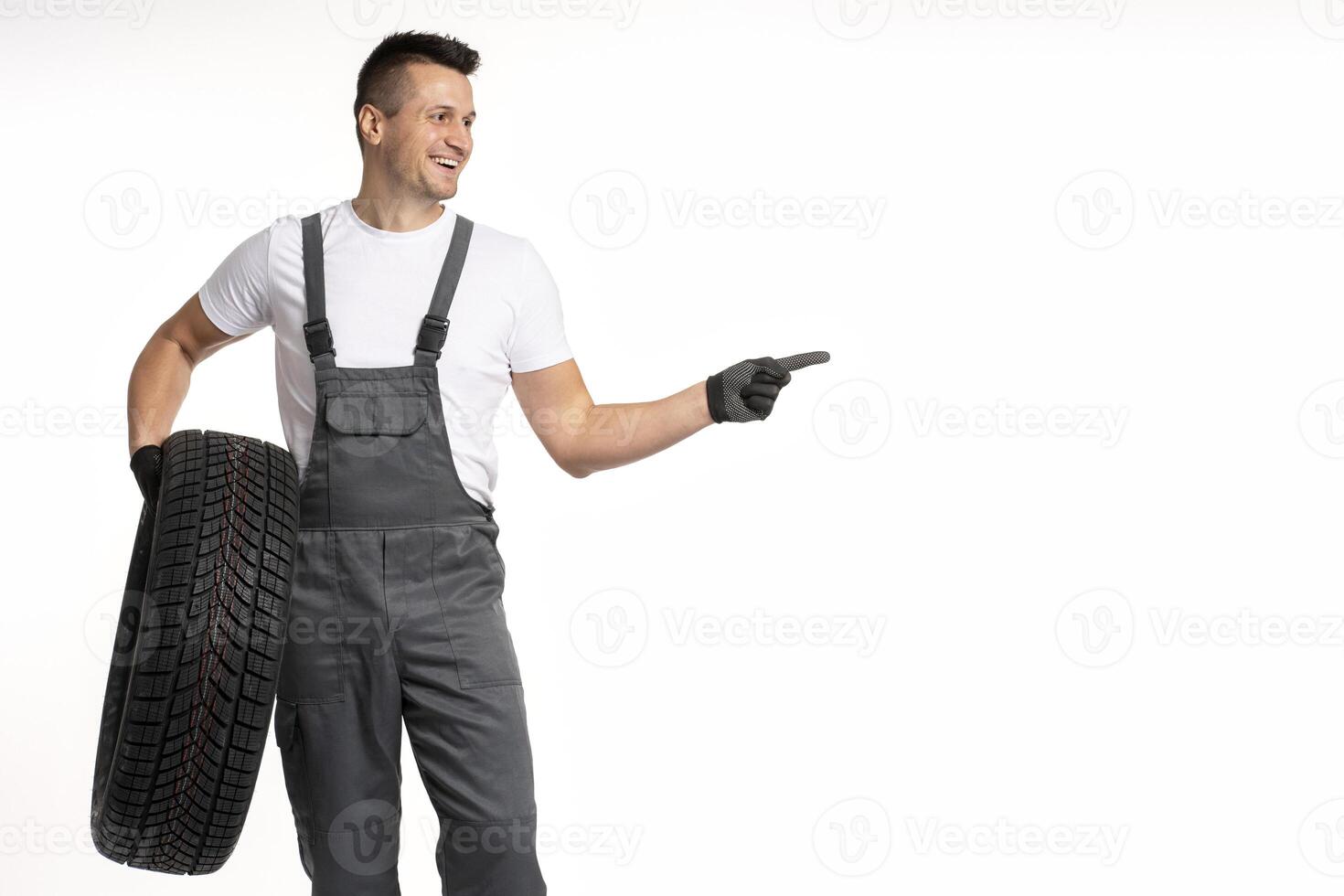 Mechanic holding tire and pointing with finger on white background photo