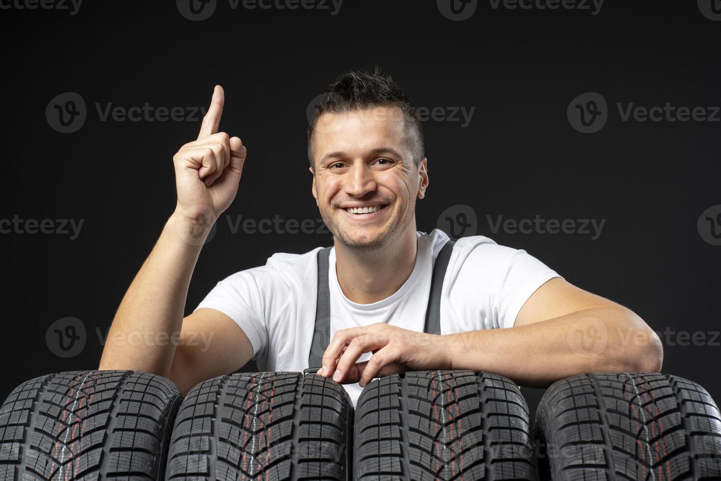 Mechanic pointing up and leaning on winter tires against black background photo
