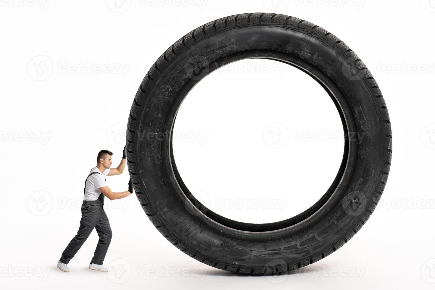 Mechanic pushing huge tire on white background photo