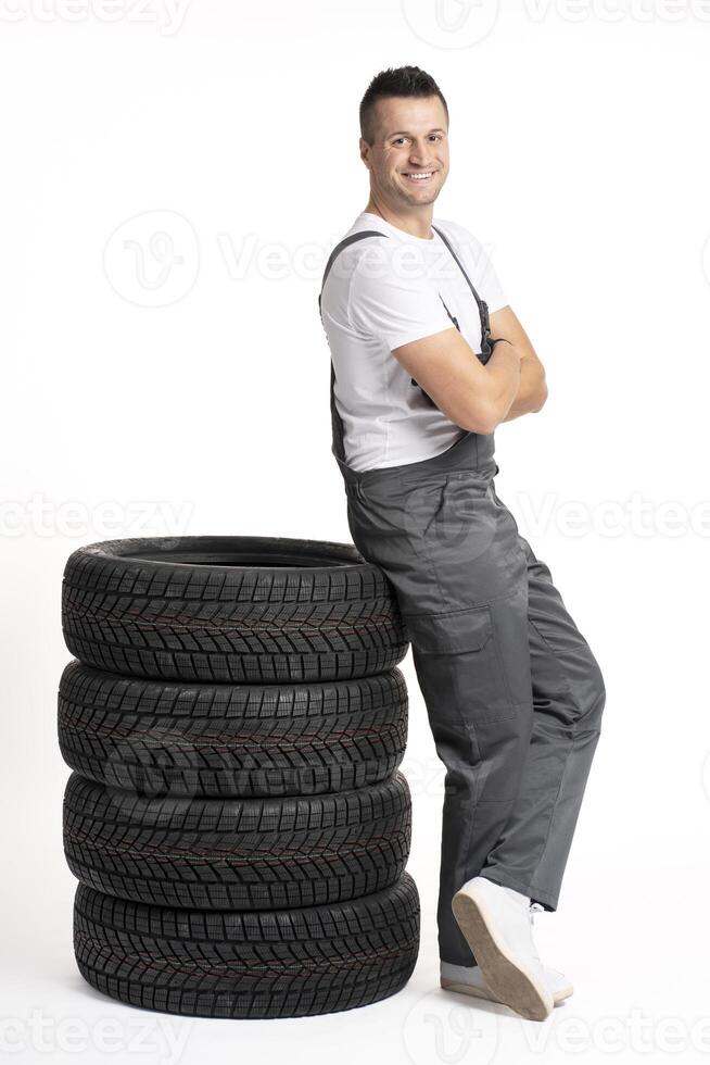 Mechanic leaning on stack of car tires with arms crossed smiling at camera photo