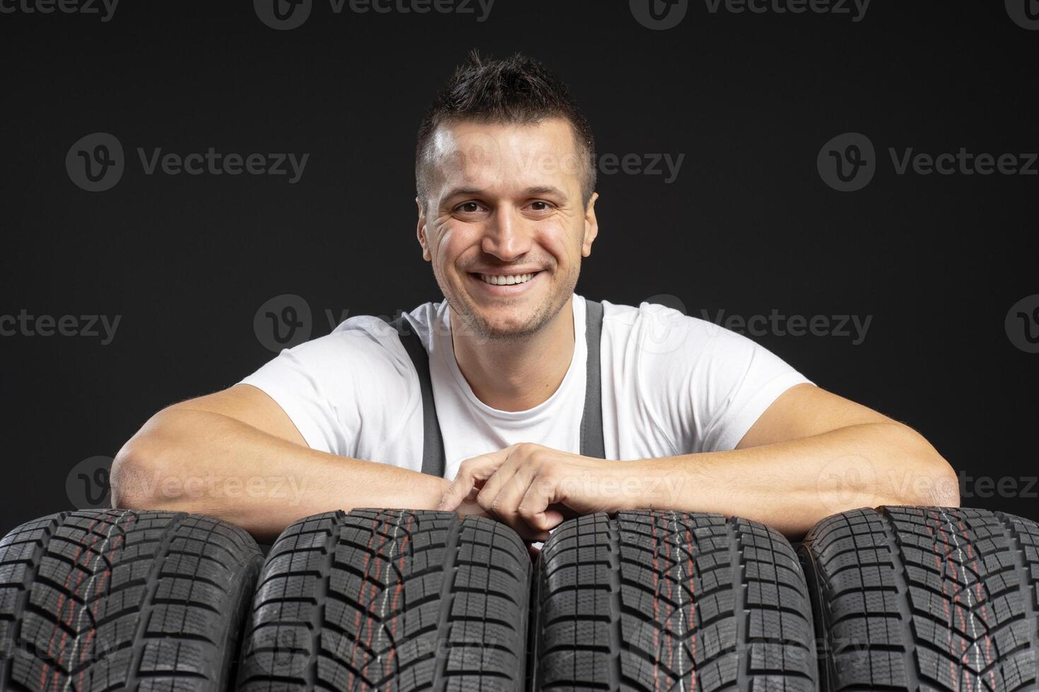 Mechanic smiling and leaning on winter tires against black background photo