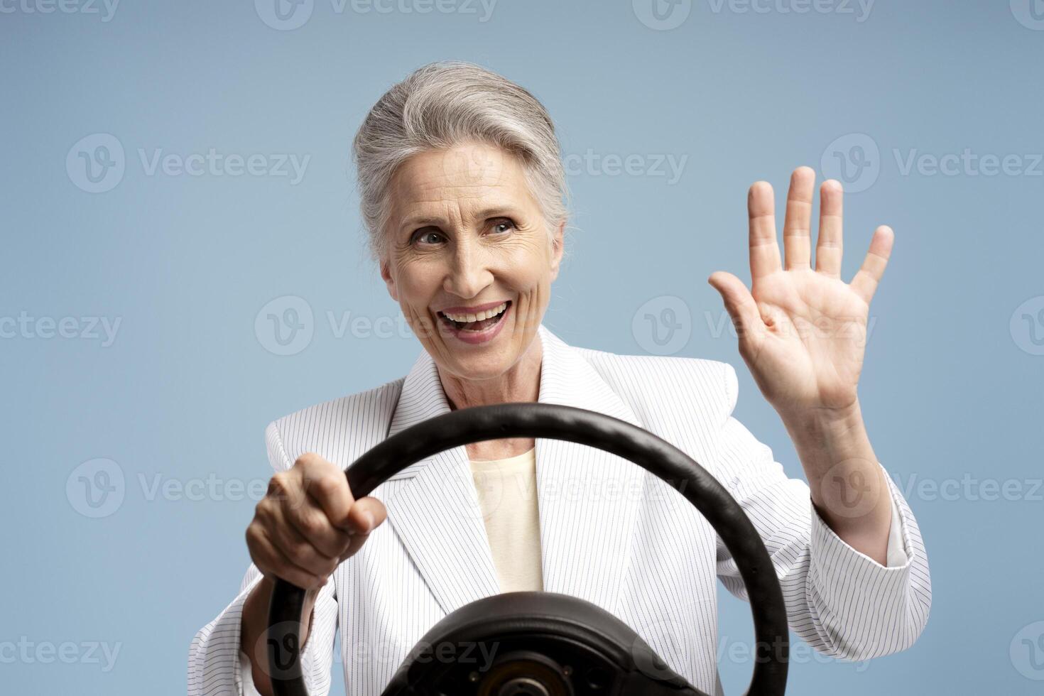 Smiling, beautiful, mature gray haired woman holding steering wheel, waving hand photo