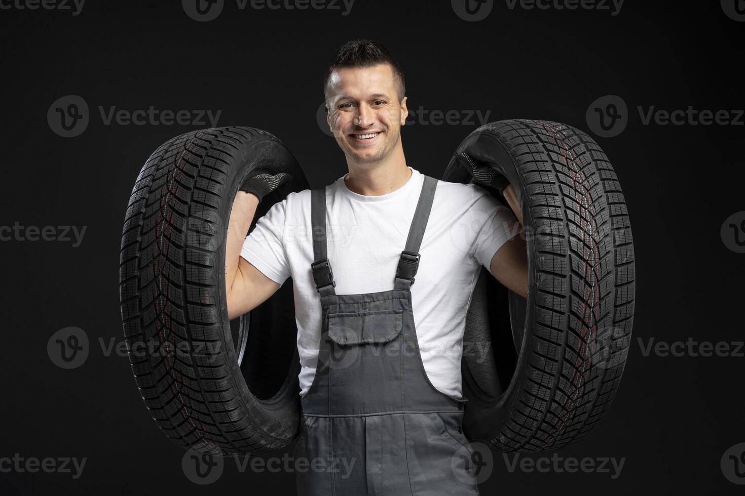 Mechanic holding two tires smiling on black background photo