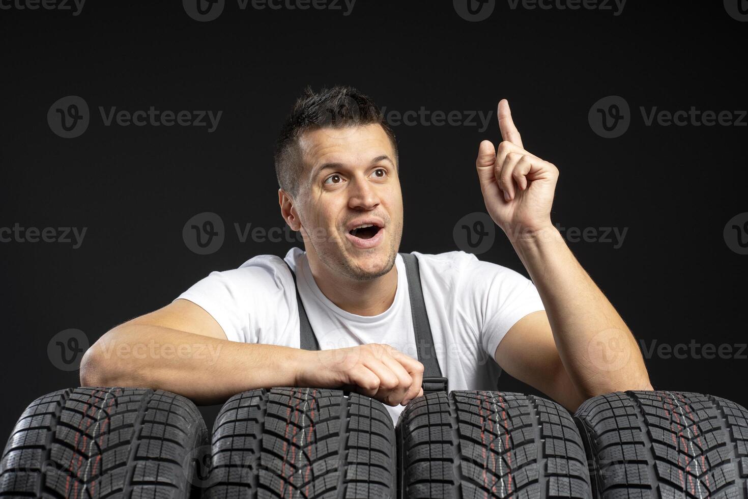 Mechanic having an idea while pointing up with car tires in the foreground photo