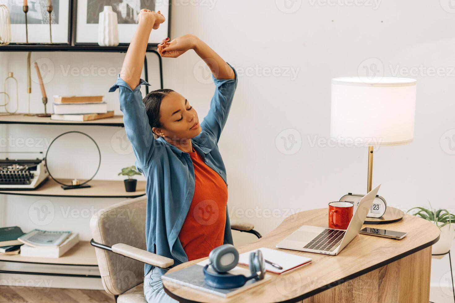 Portrait of tired, happy African American woman stretching hands up sitting at workplace photo