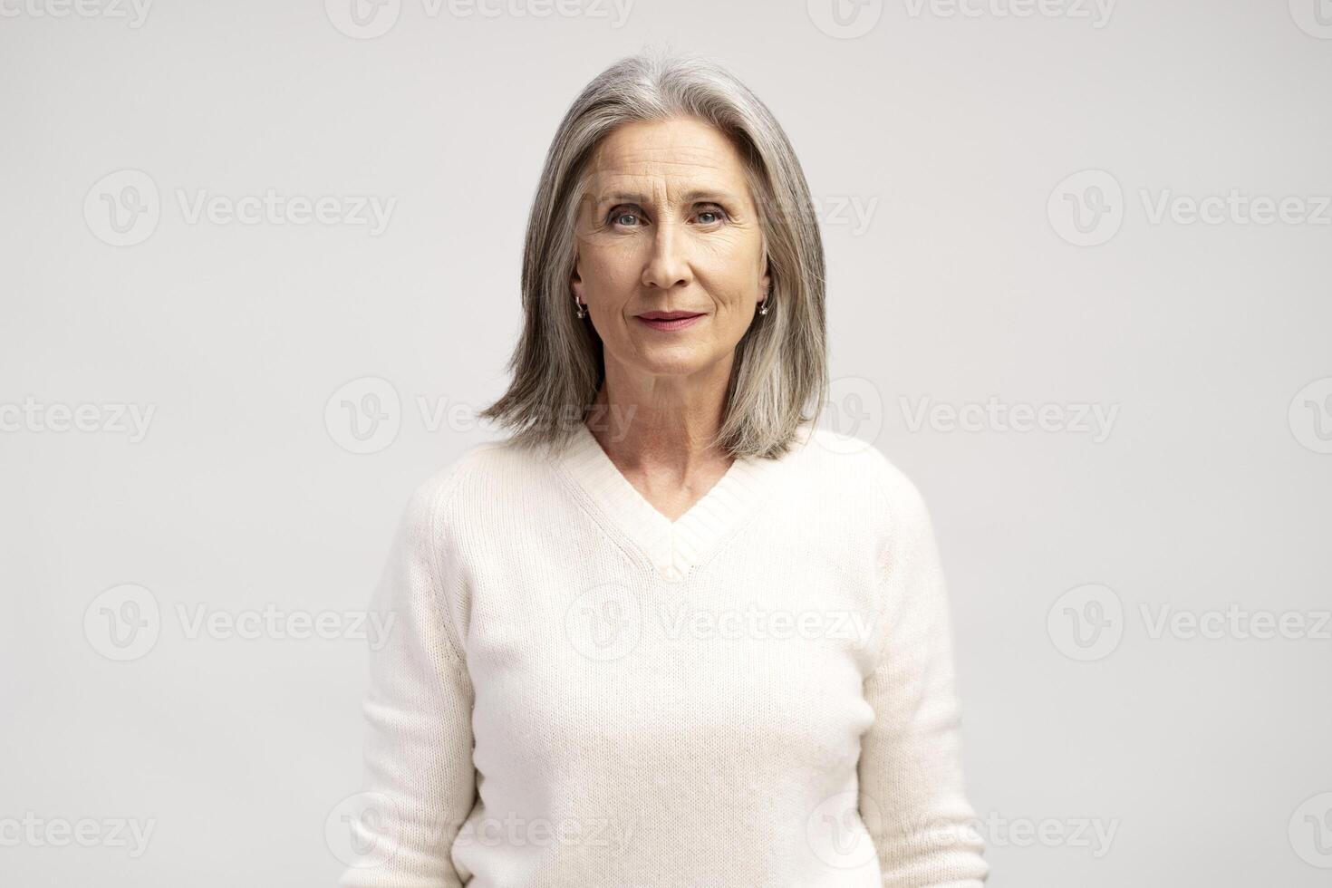 Portrait of pensive mature gray haired woman wearing white casual clothes, looking at camera photo