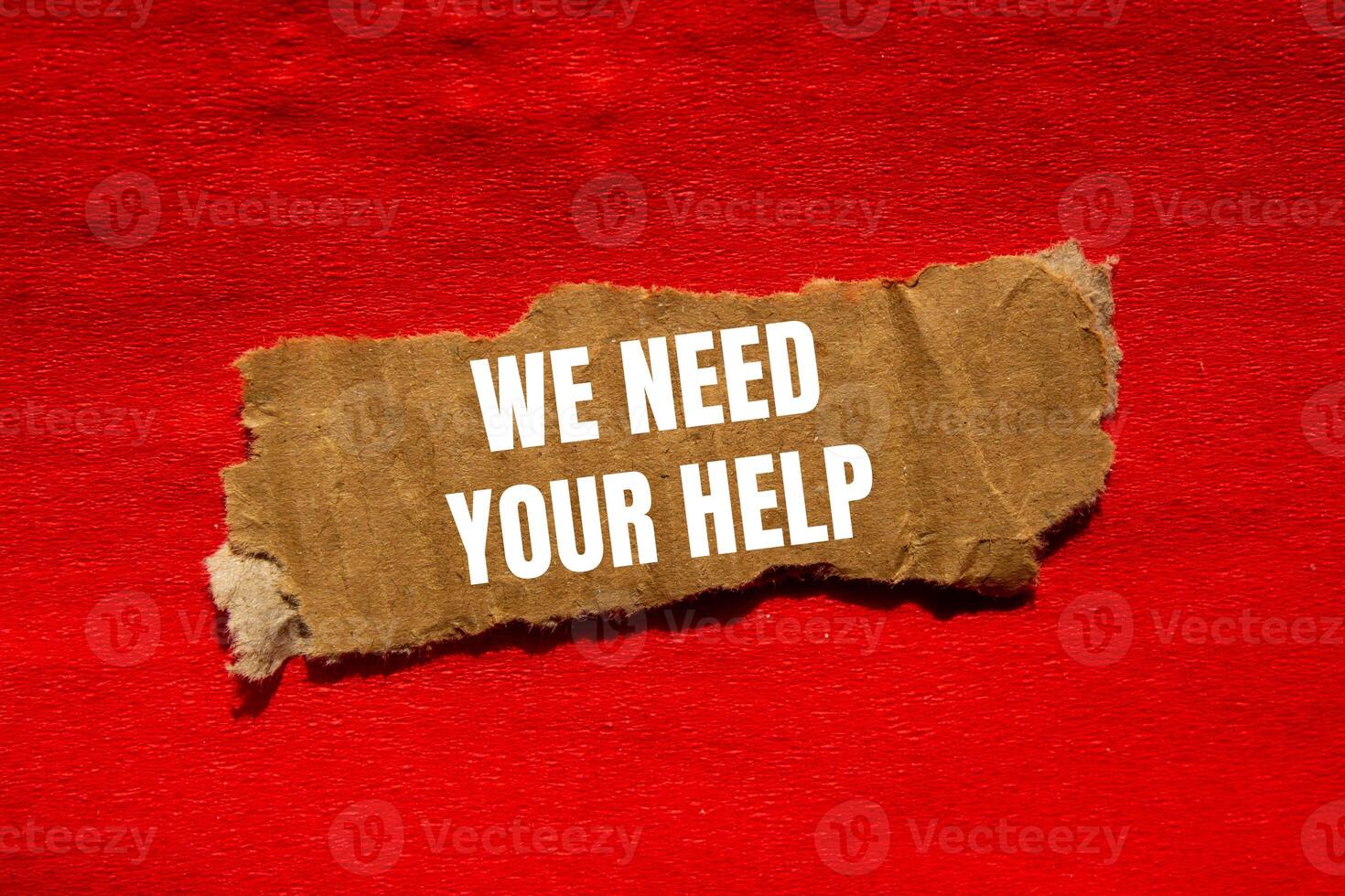 We need your help message written on ripped torn cardbaord paper piece with red background. Conceptual we need your help symbol. Copy space. photo