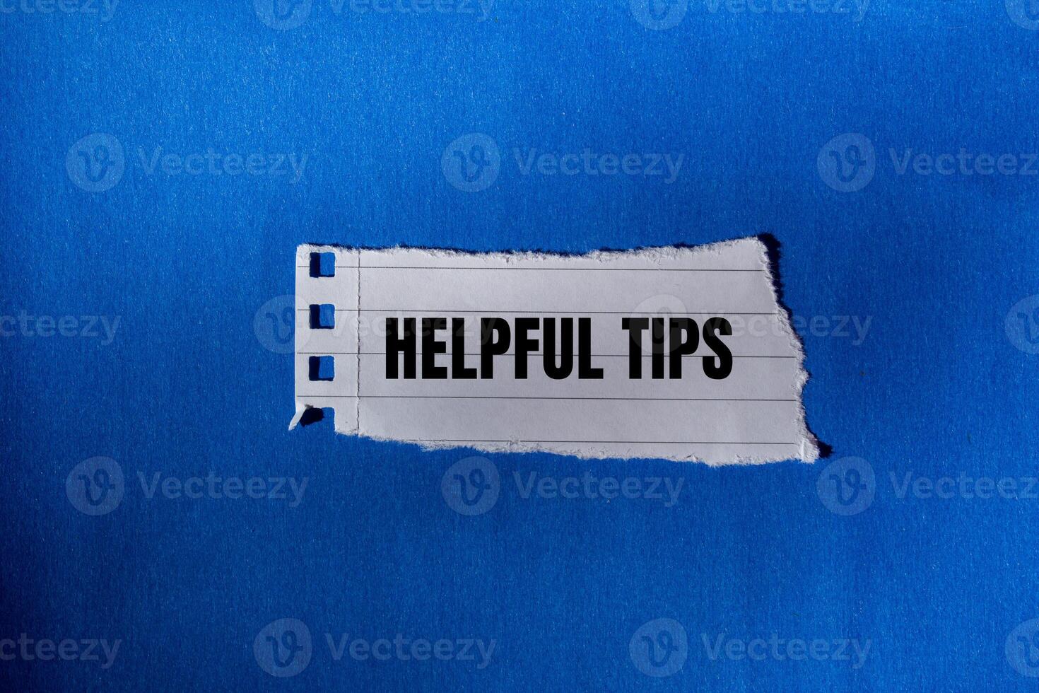 Helpful tips message written on ripped torn paper piece with blue background. Conceptual helpful tips symbol. Copy space. photo