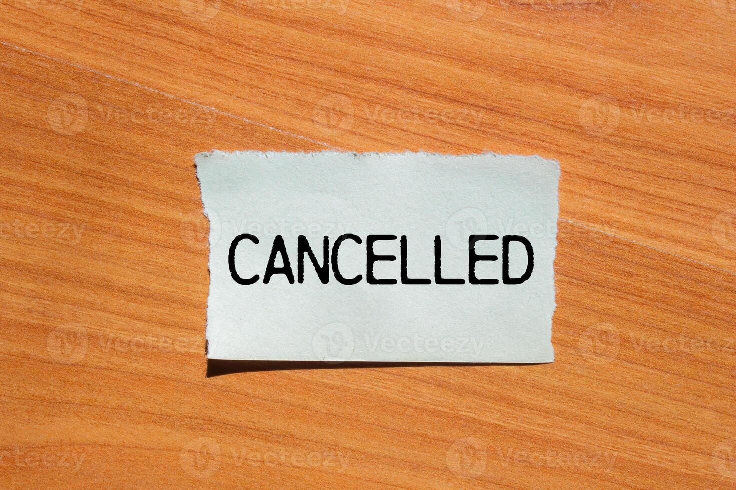 Cancelled message written on ripped torn paper piece with wooden background. Conceptual cancelled symbol. Copy space. photo