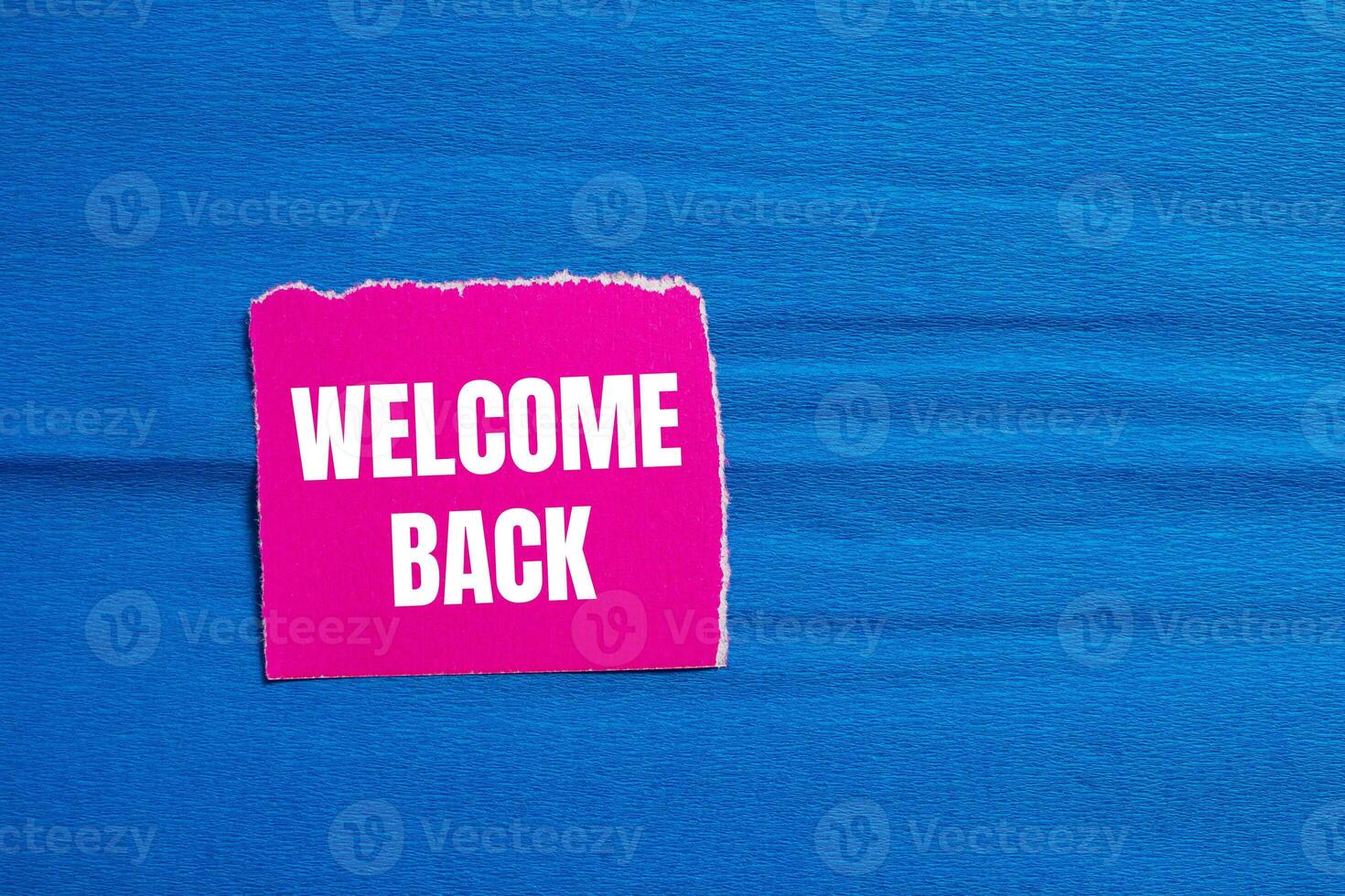 Welcome back message written on ripped pink torn paper piece with blue background. Conceptual welcome back symbol. Copy space. photo