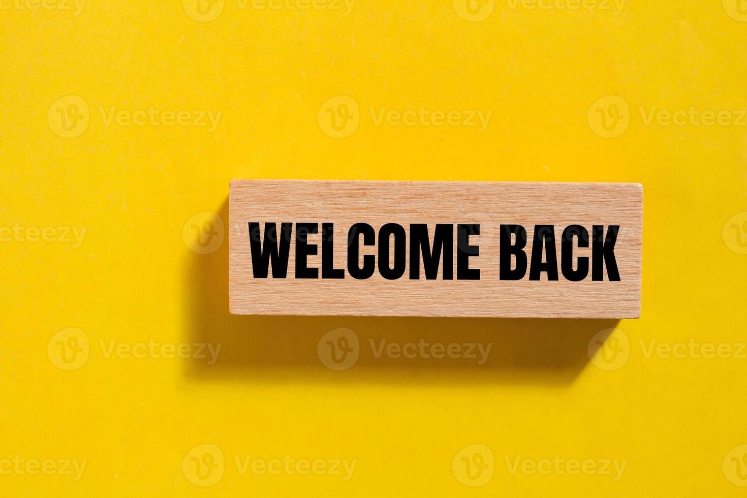 Welcome back message written on wooden block with yellow background. Conceptual welcome back symbol. Copy space. photo