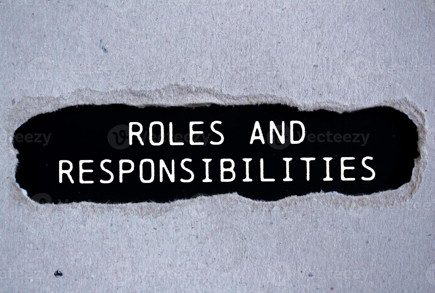 Roles and responsibilities message written on ripped torn gray paper with black background. Conceptual roles and responsibilities symbol. Copy space. photo