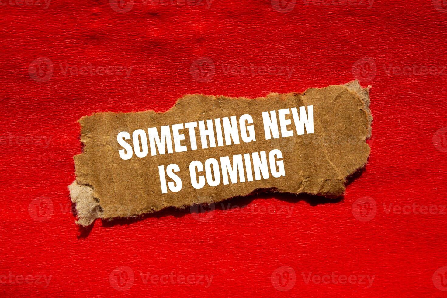 Something new is coming message written on ripped torn cardbaord paper piece with red background. Conceptual something new is coming symbol. Copy space. photo