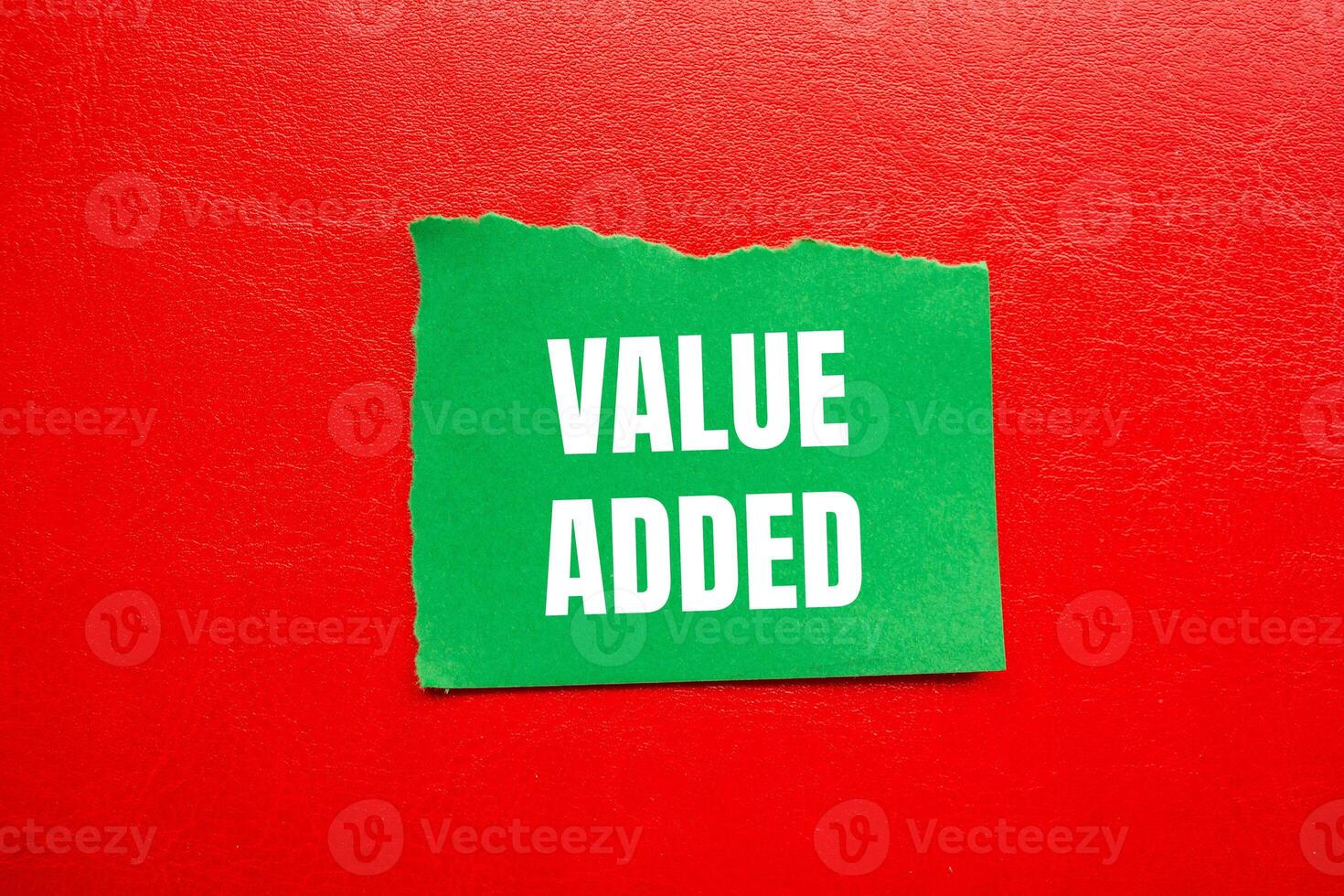Value added message written on ripped torn green paper piece with red background. Conceptual value added symbol. Copy space. photo
